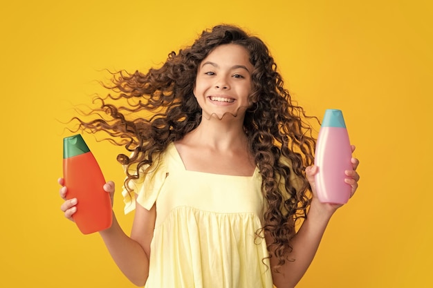 Foto gelukkig tiener portret tiener kind meisje met shampoo fles of douchegel geïsoleerd op gele achtergrond kids haar cosmetisch product glimlachend meisje