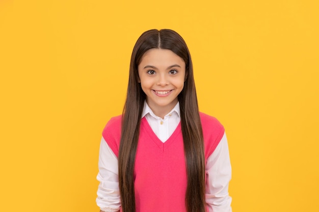 Gelukkig tiener schoolmeisje glimlachend met lang haar op gele achtergrond haarverzorging