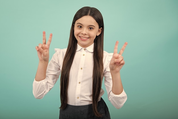 Gelukkig tienerkindmeisje toont v overwinningsteken met beide handen