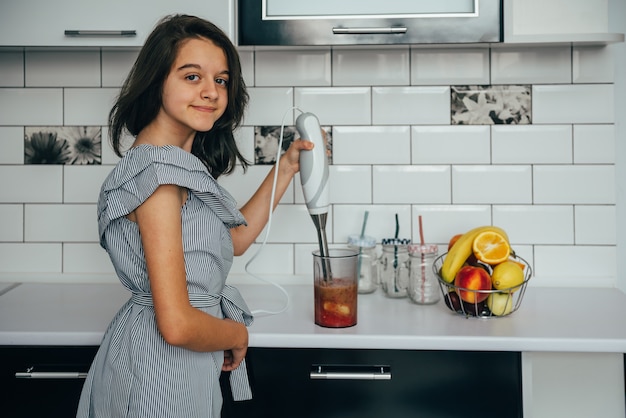 Gelukkig tienermeisje dat vers sap of maaltijd in een blender in de keuken maakt.