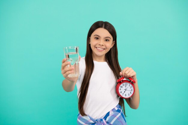 Gelukkig tienermeisje houdt een glas water en een wekker vast om gehydrateerd te blijven en de dagelijkse waterbalans op tijd te houden drink water