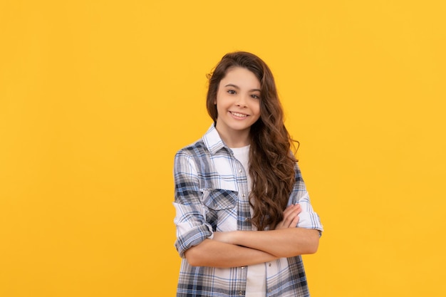 Gelukkig tienermeisje in geruit overhemd met lang krullend haar op gele achtergrond