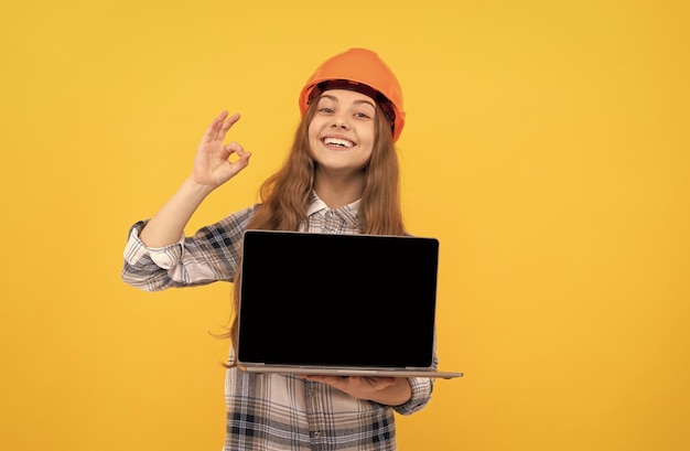 Gelukkig tienermeisje in helm en geruit overhemd die laptop ok voorstellen