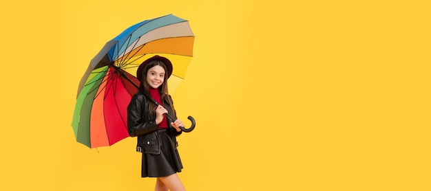 Gelukkig tienermeisje in hoed en leren kleding onder regenboogparaplu herfstweer Kind met herfstparaplu regenachtig weer horizontale posterbanner met kopieerruimte