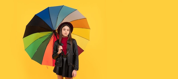 Gelukkig tienermeisje in hoed en leren kleding onder regenboogparaplu regenachtige herfst Kind met herfstparaplu regenachtig weer horizontale posterbanner met kopieerruimte