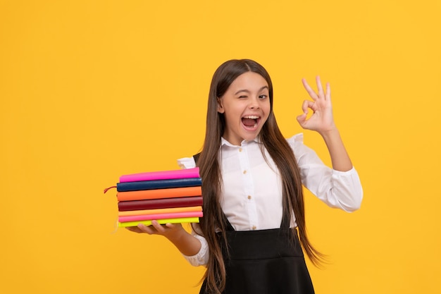 Gelukkig tienermeisje in schooluniform houd boekenstapel vast en laat goed gebaar zelfopvoeding zien