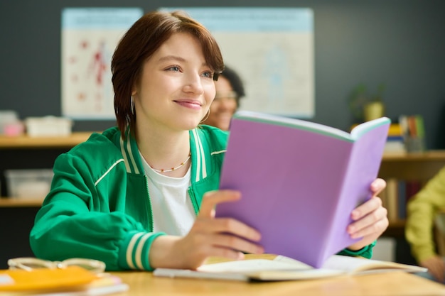 Gelukkig tienermeisje in vrijetijdskleding die naar leraar kijkt terwijl ze open schrift houdt