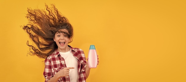 Gelukkig tienermeisje met lang krullend haar houdt shampoo fles schoonheid Banner van kind meisje haarverzorging studio poster koptekst met kopie ruimte