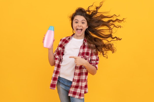 Gelukkig tienermeisje met lang krullend haar houdt shampoofles leuk vast