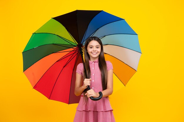 Gelukkig tienermeisje met regenboog paraplu staande geïsoleerd op gele achtergrond geïsoleerd op wit Vrolijke tiener kind houdt parasol zomerjurk