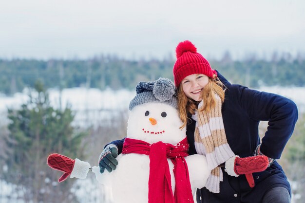 Gelukkig tienermeisje met sneeuwman in de winterbos