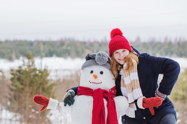 Gelukkig tienermeisje met sneeuwman in de winterbos