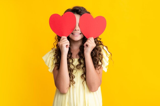 Gelukkig tienerportret Vrolijk mooi romantisch tienermeisje houdt rood hartsymbool van liefde voor Valentijnsdag geïsoleerd op gele achtergrond Glimlachend meisje