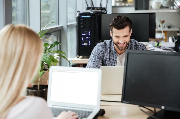 Foto gelukkig twee collega's in kantoor naaien tijdens het gebruik van laptops