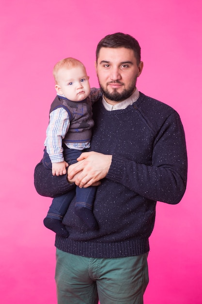 Gelukkig vader bedrijf zoontje in handen over roze muur