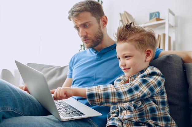 Gelukkig vader en zoon zittend op de bank en kijken naar iets op laptop