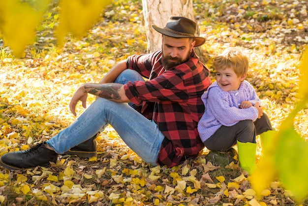 Gelukkig vader en zoon zittend op gevallen gele herfstbladeren.