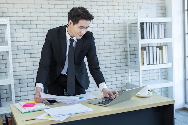 Gelukkig van succesvolle Aziatische jonge zakenman hebben benadrukt, zie het document businessplan en laptopcomputer op houten tafel Op de achtergrond van de kantoorruimte