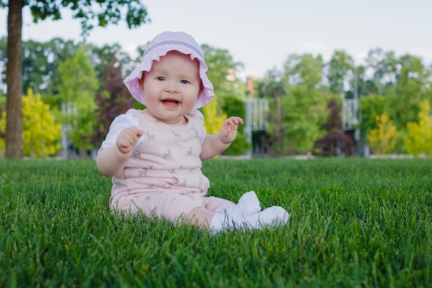 Gelukkig verpleging babymeisje zittend op het gras in het park en glimlachend op een zonnige zomerdag