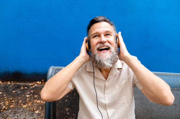 Gelukkig volwassen blanke man met grijze baard luisteren naar muziek met koptelefoon buitenshuis Lifestyle