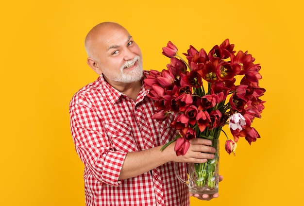 Gelukkig volwassen gepensioneerde man met baard houden tulp lentebloemen op gele achtergrond