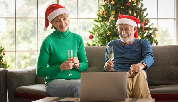 Gelukkig volwassen vrouw en bejaarde man met glazen champagne glimlachend en kijken naar video op laptop zittend op de bank en kerst thuis vieren