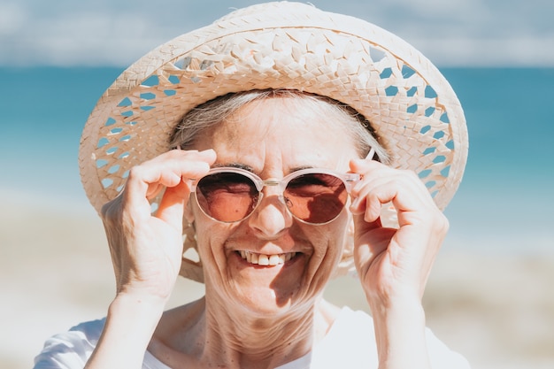 Gelukkig volwassen vrouw van 50 jaar op het strand met trendy zonnebril en een hoed