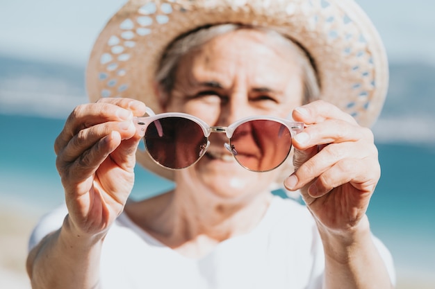 Gelukkig volwassen vrouw van 50 jaar op het strand met trendy zonnebril en een hoed