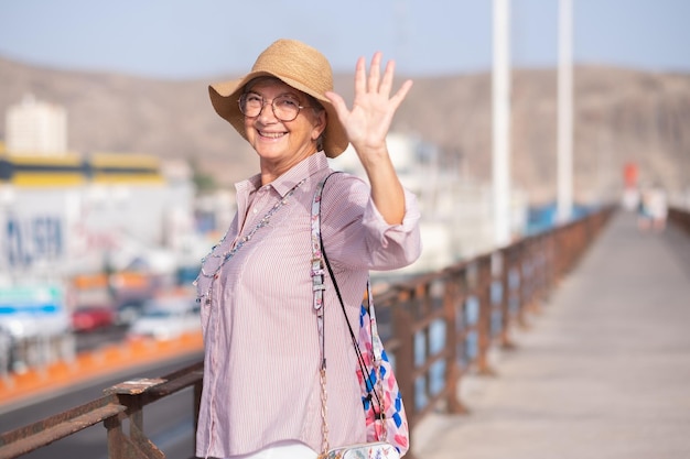 Gelukkig volwassen vrouwelijke reiziger met hoed zwaaiende hand kijkend naar camera tijdens het aan boord gaan van de veerboot in de haven voor vertrek weekend of vakantie concept