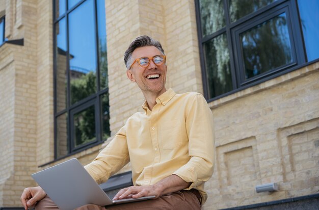 Gelukkig volwassen zakenman met behulp van laptop, typen op toetsenbord, lachen