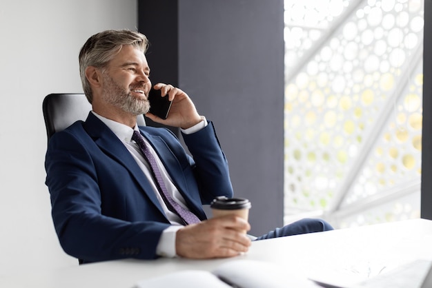 Gelukkig volwassen zakenman met werkpauze praten op mobiele telefoon en koffie drinken