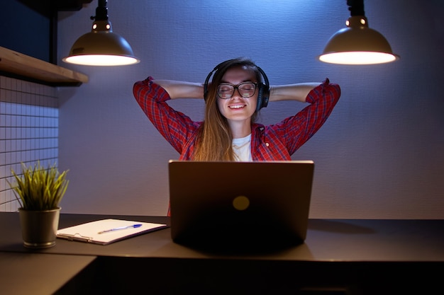 Gelukkig vreugdevolle tevreden vrouw muziekliefhebber in draadloze hoofdtelefoons met handen achter je hoofd genieten van en luisteren naar ontspannende muziek online met behulp van een laptop