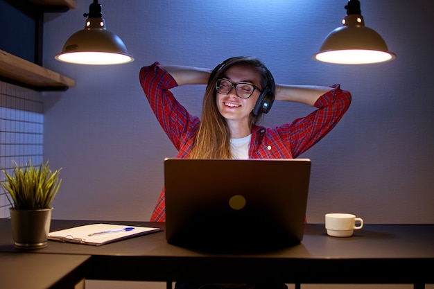 Gelukkig vreugdevolle tevreden vrouw muziekliefhebber in draadloze hoofdtelefoons met handen achter je hoofd genieten van en luisteren naar ontspannende muziek online met behulp van een laptop