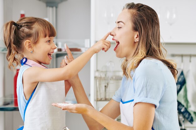 Foto gelukkig vrij jonge vrouw en haar dochtertje spelen met bloem bij het bakken van gebak in de keuken