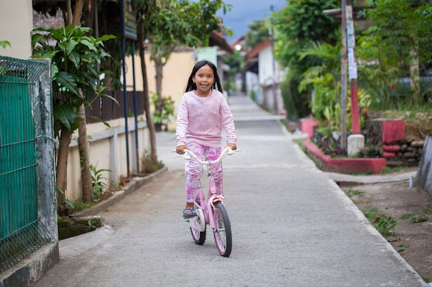 Gelukkig vrolijk Aziatisch kindmeisje dat een fiets berijdt