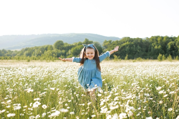 Gelukkig vrolijk kindmeisje draagt een stijlvolle, rustieke jurk die in de weide met bloemen over de natuur wordt uitgevoerd