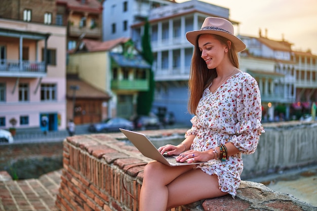 Gelukkig vrolijk lachend mooi schattig vrolijk jong meisje met laptop buitenshuis in de stad Tbilisi