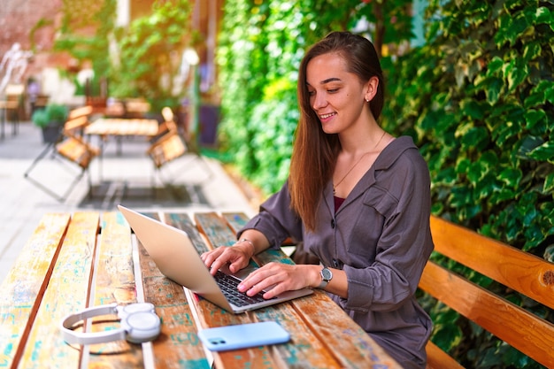 Gelukkig vrolijk lachend mooi schattig, vrolijk jong millennial freelancer-meisje dat laptop gebruikt voor online werken op afstand in groen café