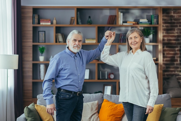 Gelukkig vrolijk senior getrouwd stel dat plezier heeft thuis oudere familie danst grijsharige gepensioneerden verheugen zich in het verplaatsen van actieve levensstijl oude man en vrouw brengen vrije tijd binnenshuis door, luisteren naar muziek