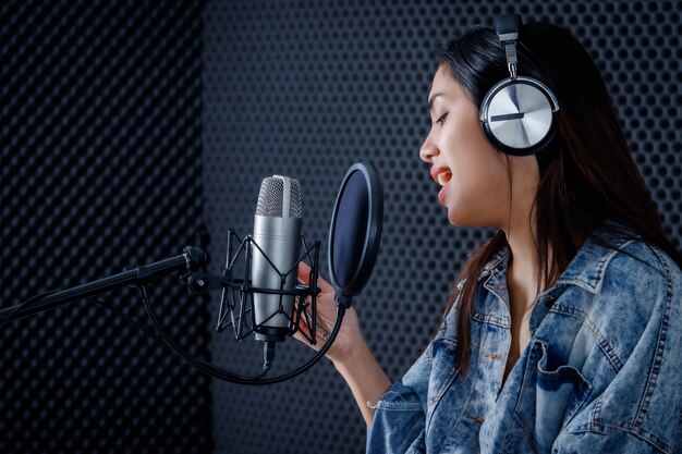 Gelukkig vrolijke mooie glimlach van portret van jonge aziatische vrouw kijk naar de zanger van de smartphone die een koptelefoon draagt die een nummer van de microfoon opneemt in een professionele studio