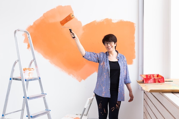 Gelukkig vrouw van middelbare leeftijd schilderen binnenmuur met verfroller in nieuw huis. Een vrouw met roller verf op een muur toe te passen.