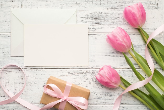 Gelukkig vrouwendagconcept. Foto van een boeket met tulpen verpakte geschenkdoos en witte lege lege kaart voor tekstontwerp op houten wit bureau