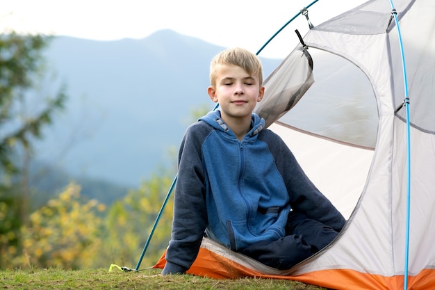 Gelukkig wandelaar kind jongen rust in een toeristische tent op bergcamping