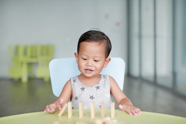 Gelukkig weinig aziatische babyjongen die het spel van de houtsnedentoren voor hersenen en fysieke ontwikkelingsvaardigheid spelen in een klaslokaal. focus op het gezicht van kinderen. kid verbeelding en leren concept.