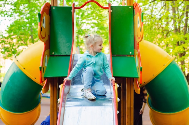 Gelukkig weinig blondemeisje die pret op een speelplaats op een de zomerdag hebben in een zonnig stadspark.