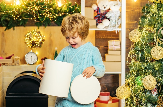 Gelukkig weinig jongenskind met heden of giftdoos binnenshuis. Gelukkig schattig kind in kerstmuts met heden