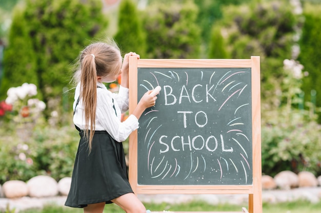 Gelukkig weinig schoolmeisje met een schoolbord buiten