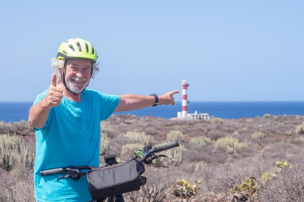 Gelukkig witharige actieve seniorman off-road fietsen met elektrische fiets op zee oudere blanke man in zomervakantie vuurtoren aan de horizon