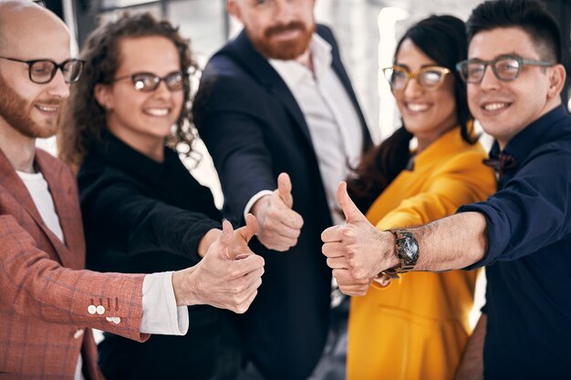 Gelukkig zakelijk team. Groep vrolijke zakenmensen in vrijetijdskleding die dicht bij elkaar staan en hun duimen opsteken. selectieve focus