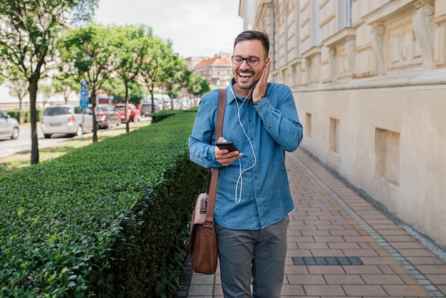 Gelukkig zakenman genieten van muziek via een koptelefoon op slimme telefoon in de stad